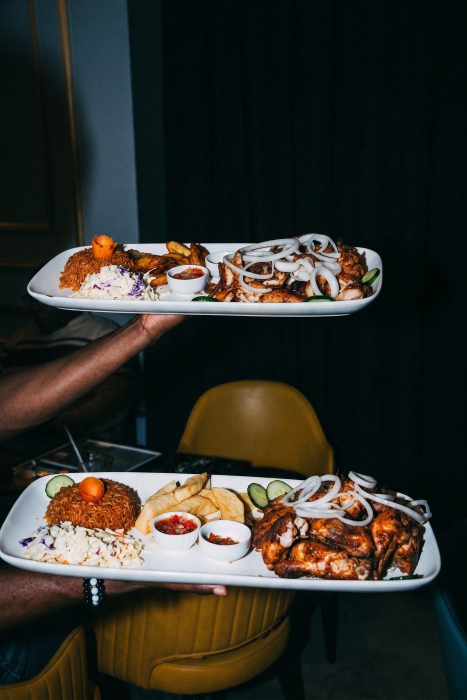 Two plates of rice and chicken carried to a table