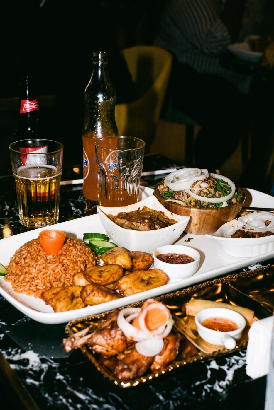 Platters of jollof rice, plantain and chicken with drinks